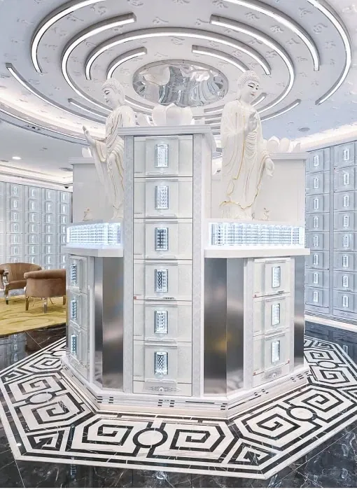 A tiered memorial tower of pale niches beneath sculpted figures, standing on a patterned marble floor