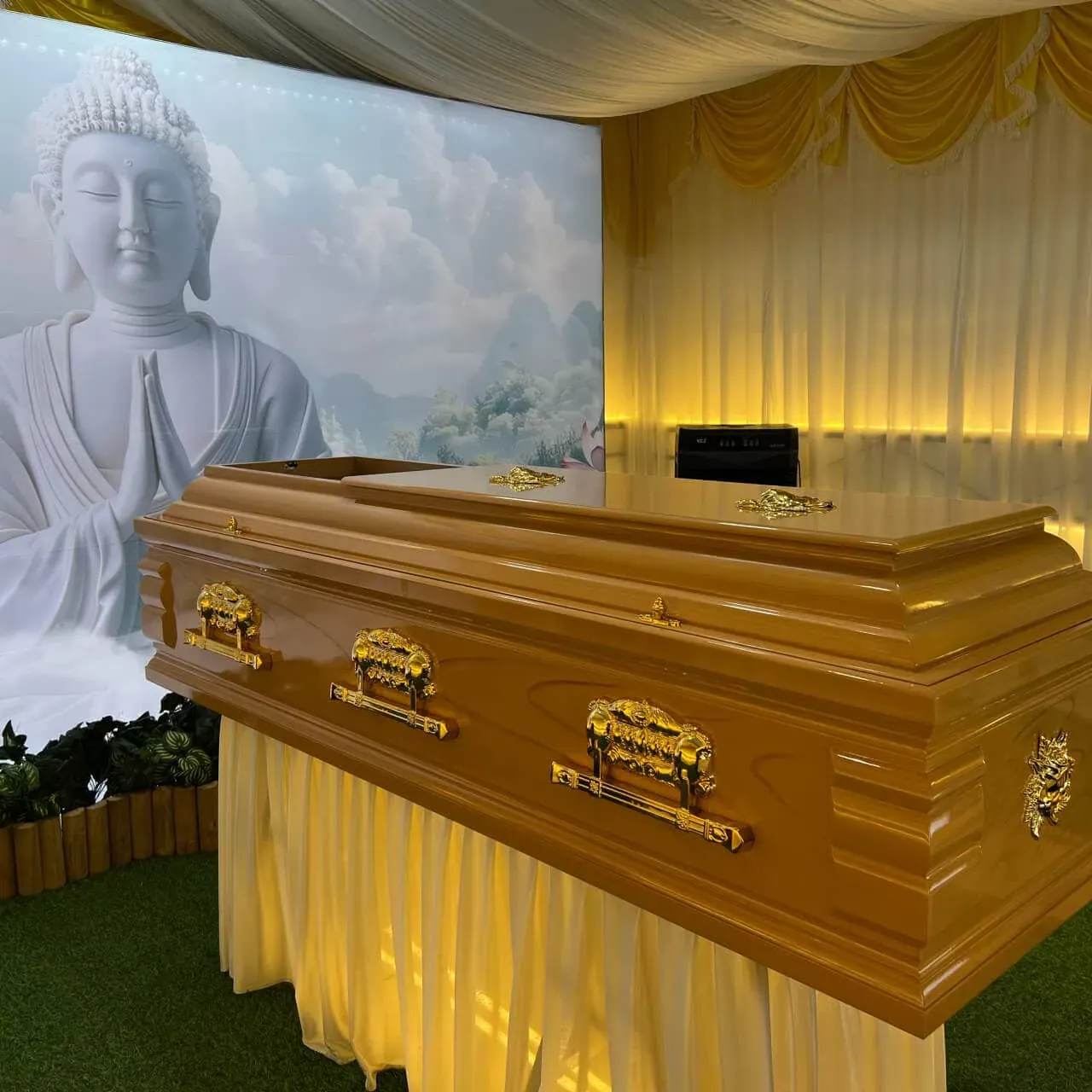 A polished wooden casket before a draped backdrop and a large seated figure